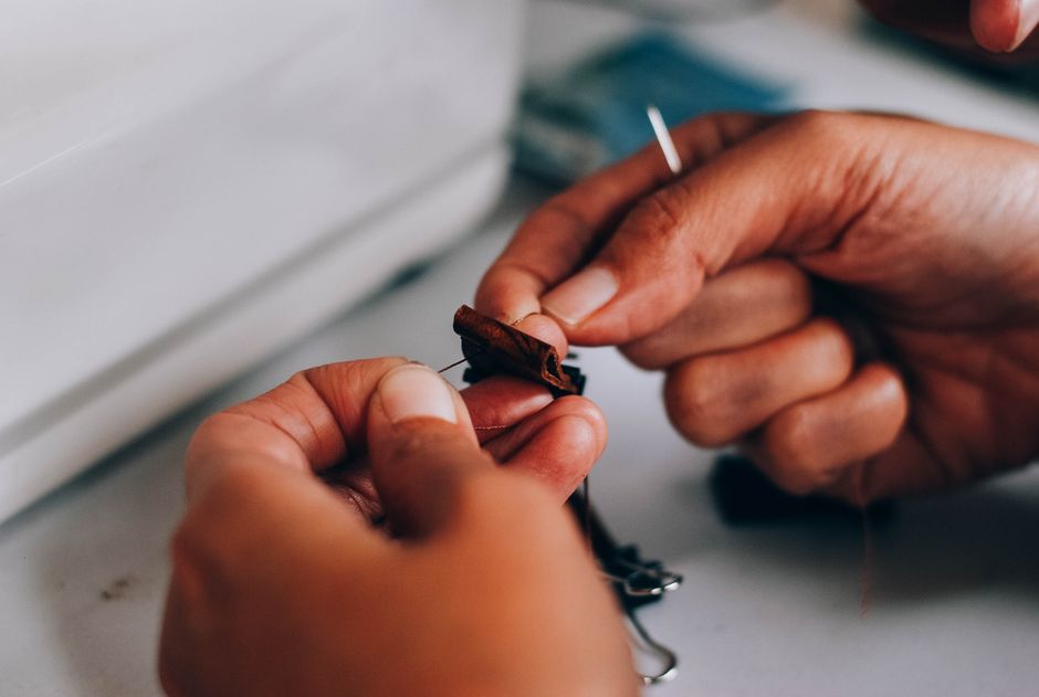 Detailed macro shot of hands threading a needle through fabric, showcasing intricate sewing technique.