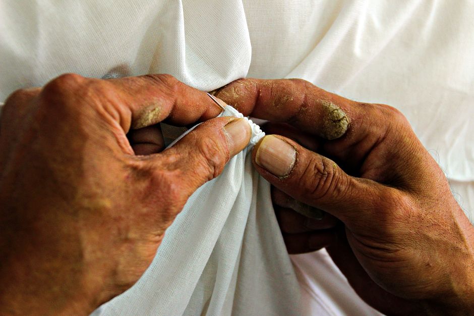 Detailed view of hands carefully sewing a white fabric with a needle.